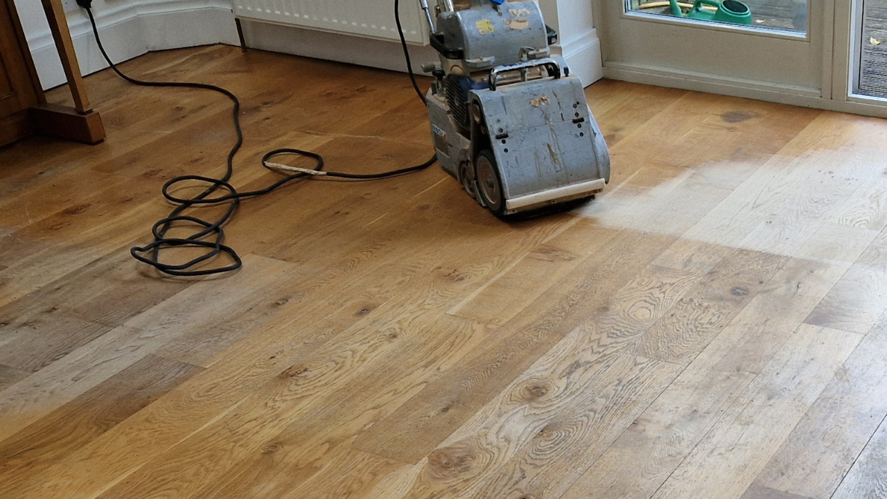 Professional Wood Floor Sanding machine halfway across an engineered oak floor, clearly showing the lighter, freshly sanded boards beside the darker worn surface.