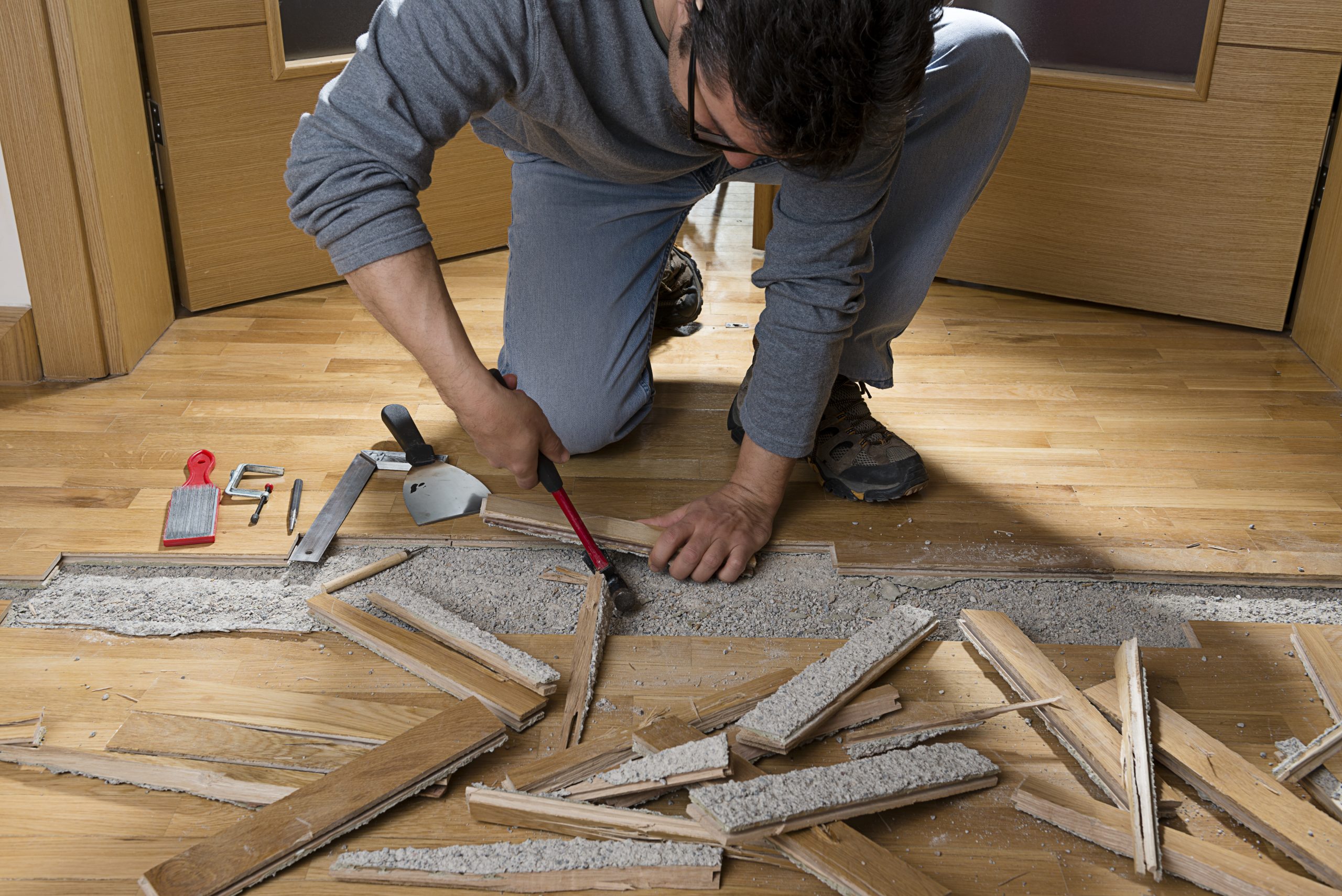 Professional Wood Floor Sanding specialist removing damaged boards from an oak strip hardwood floor during the repair phase.