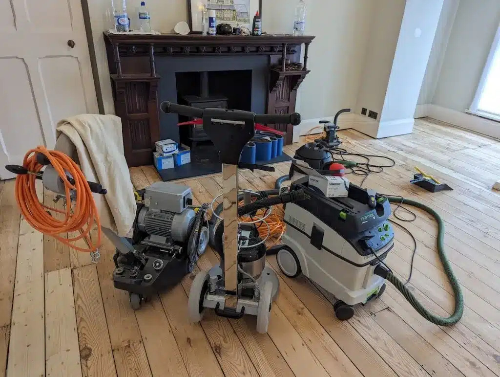 Wood Floor Sanding equipment—including drum sander, buffer and industrial vacuum—set up on partially sanded solid pine floorboards ready for refinishing.