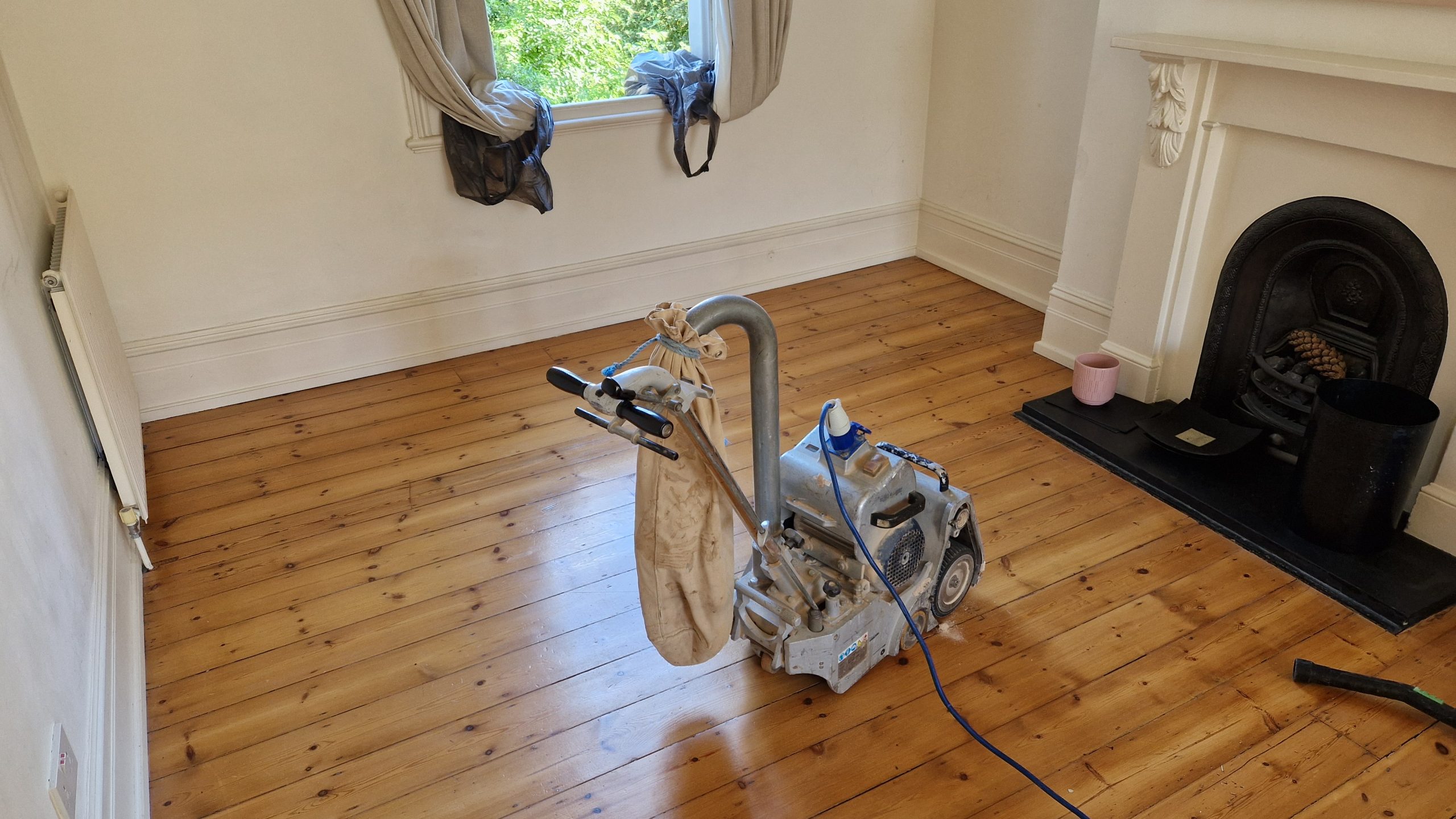 Wood Floor Sanding of dust-free softwood pine floorboards with a drum sander and dust-collection bag.