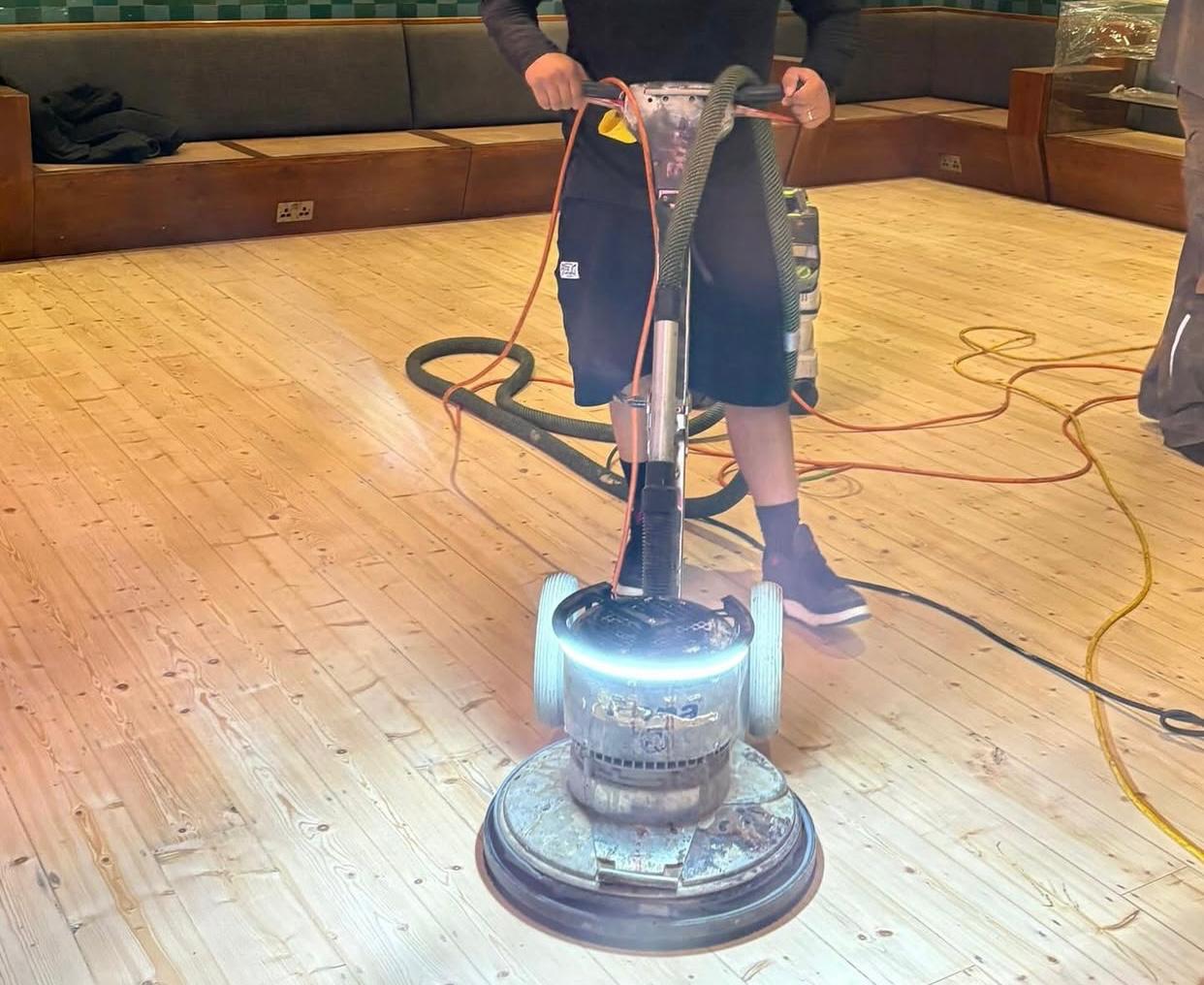 Wood Floor Sanding of softwood pine floorboards underway with a rotary buffer and dust-extraction hose.