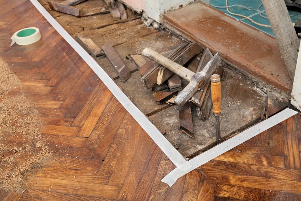 Floor Sanding Preparation Checklist showing repair work on dark oak herringbone parquet floor at a doorway threshold.