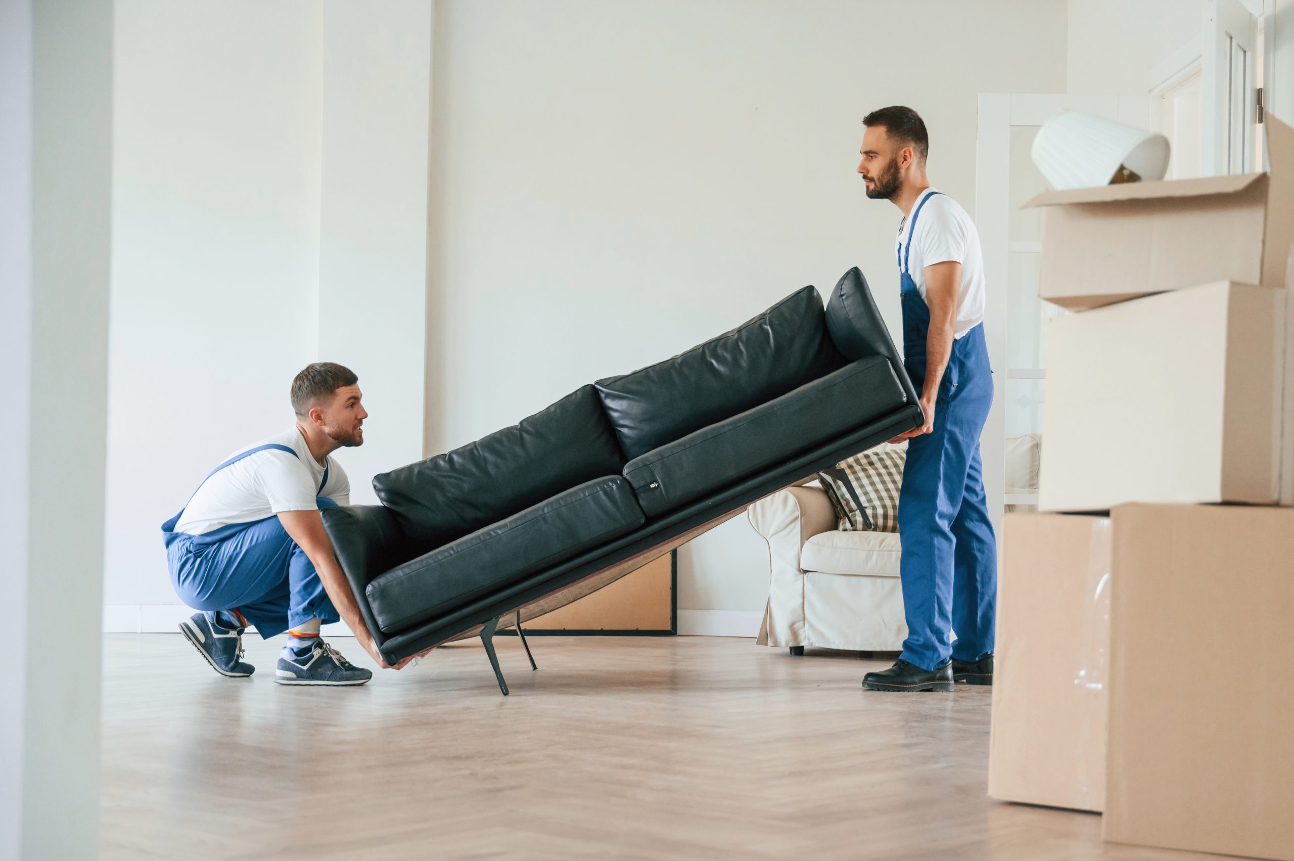 Floor Sanding Preparation Checklist step as two workers lift a sofa to clear an oak plank wood floor before sanding.