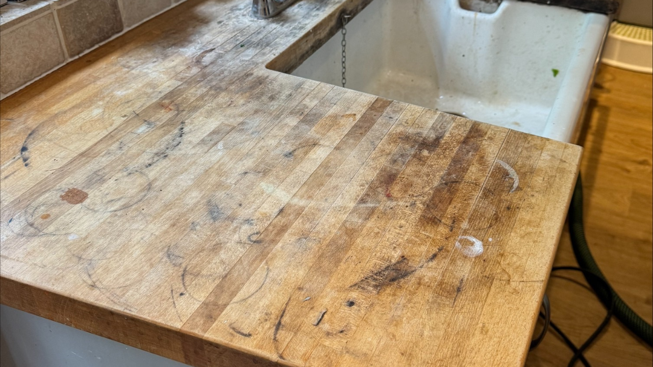 Worktop Refinishing on an oak butcher block wooden worktop before restoration, showing heavy staining, ring marks and scratches next to an oak wood floor.
