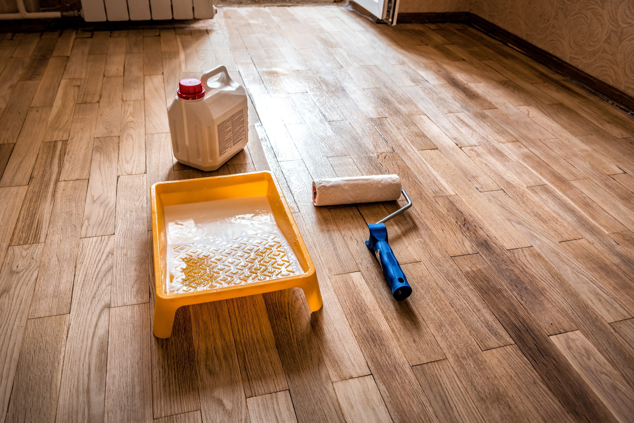 Hardwood Floor Refinishing setup showing a roller, paint tray and sealant ready to apply a protective coat to a light oak block hardwood floor for a smooth, luxury finish.